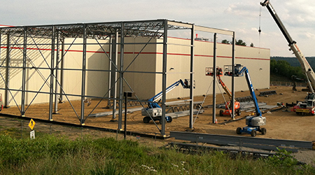 Photo of several cranes and the start of building a new warehouse.