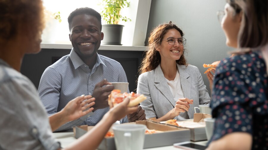 Four people sitting around a table in office attire, and eating pizza.