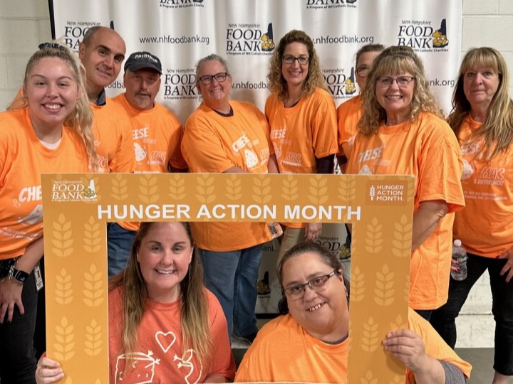 Ten people standing next to each other  displaying a sign for the New Hampshire Food Bank organization.