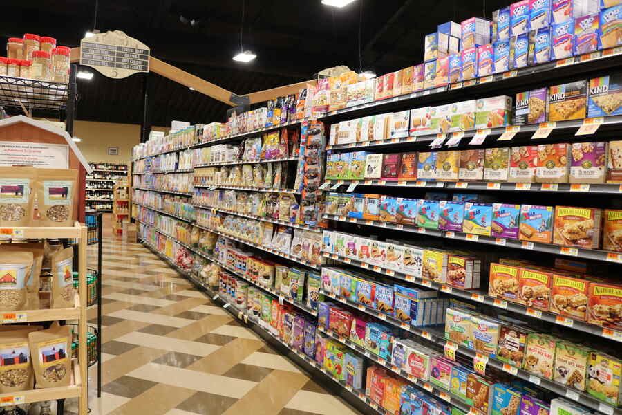 Long range point of view of a grocery aisle stocked with various types of granola and cereal products.